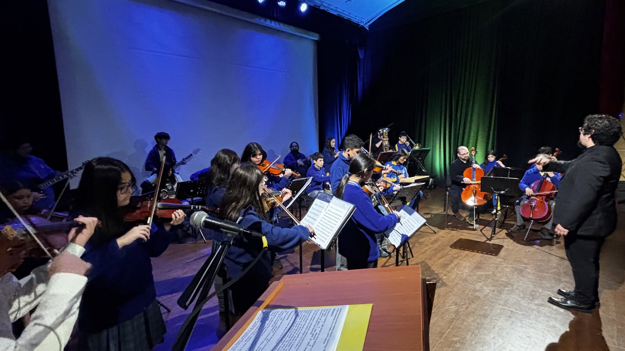 Estudiantes del colegio interpretando música en un escenario junto a su director